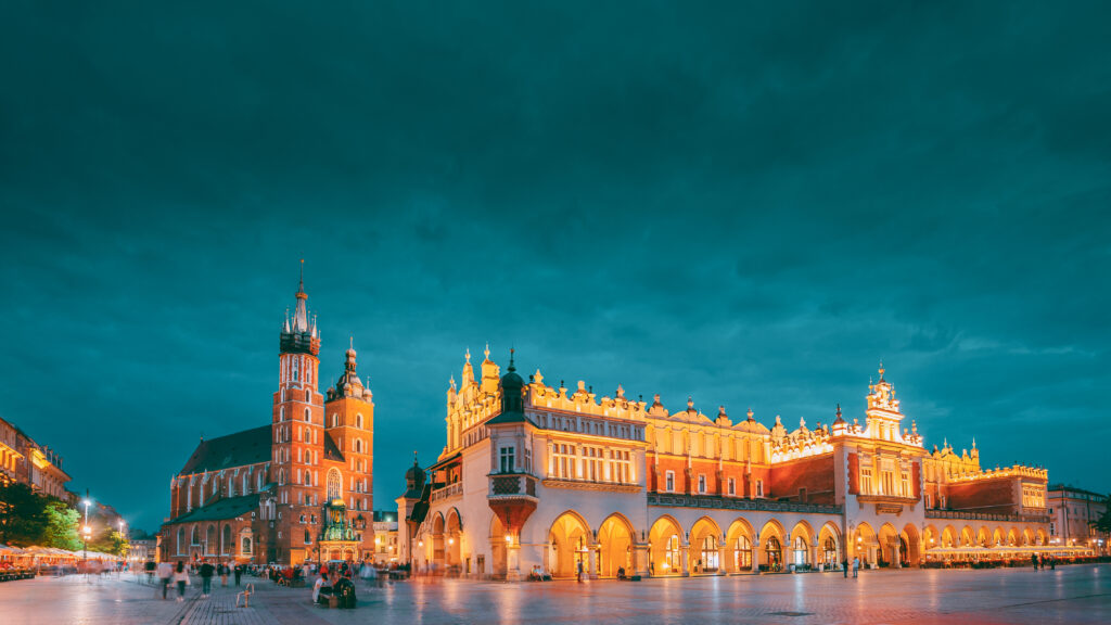 Krakow, Poland. Evening Night View Of St. Mary's Basilica And Cloth Hall Building. Famous Old Landmark Church Of Our Lady Assumed Into Heaven. UNESCO World Heritage Site Sukiennice Kraków
